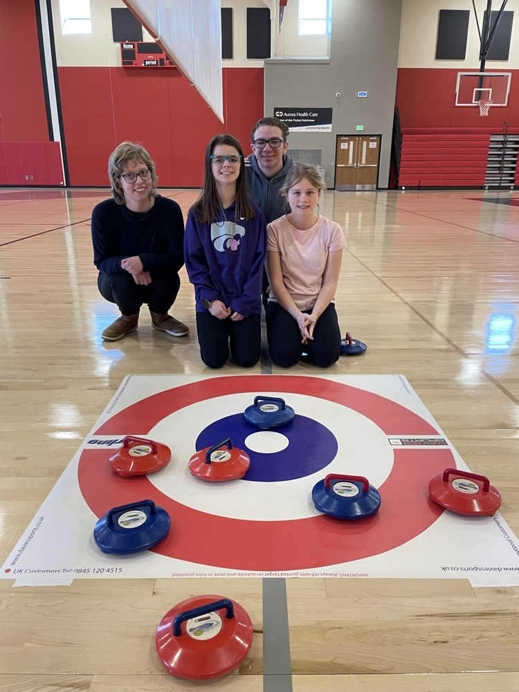 students in the gym posing with curling stones 