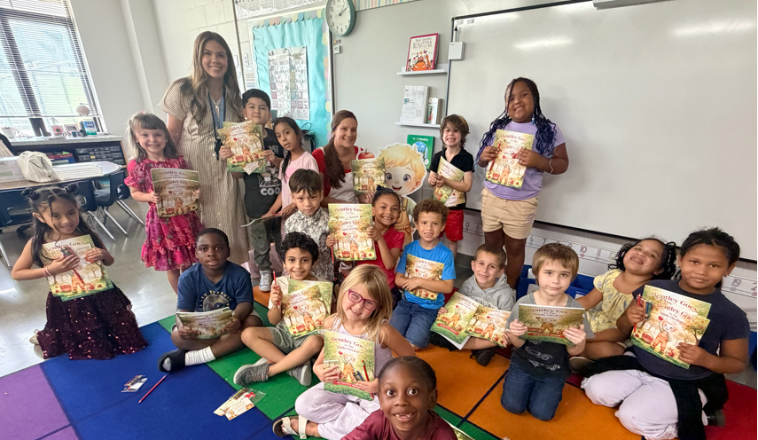 Mrs. Porter's first grade class with author Ray Marie smiling and showing their new books they received!