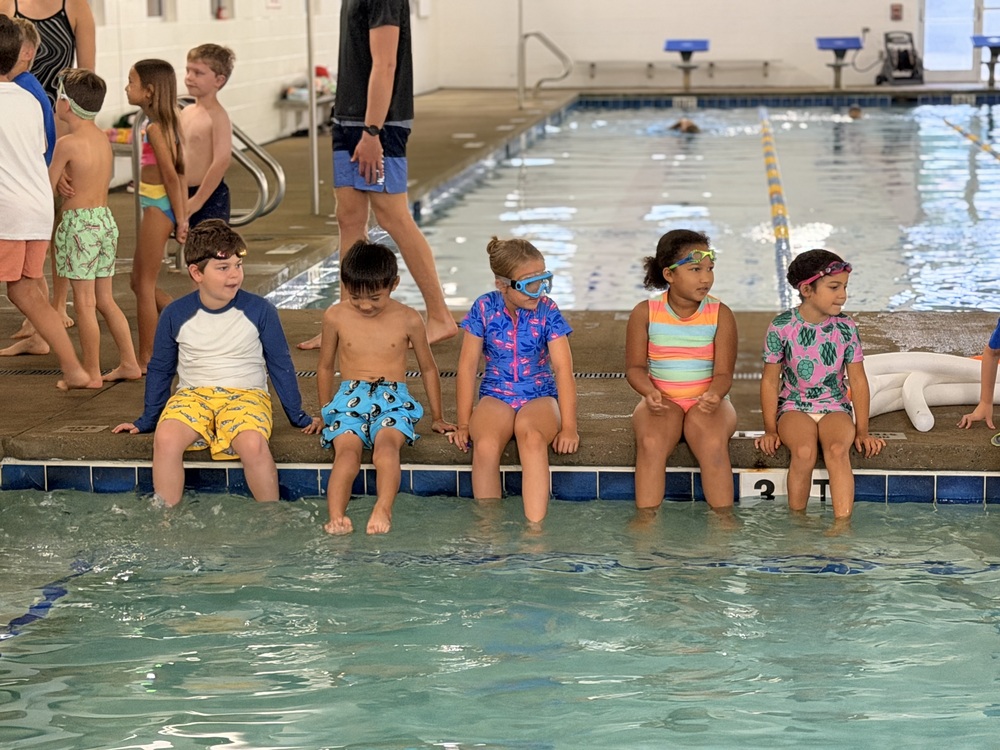second grade students sitting on the edge of the pool for swimming lessons