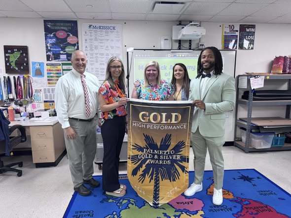 Image shows Dr. Merck and McKissick administrators holding the Palmetto Gold Award banner.   