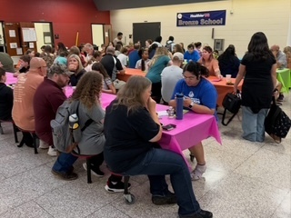 **ADA-compliant alt text:**  “Parents and school staff gather around tables in a school cafeteria for a parent engagement event, with participants talking and sharing information.”