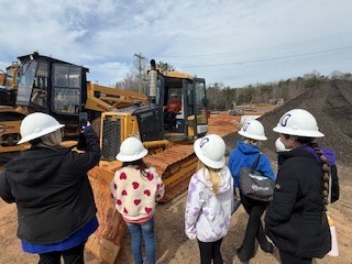 Students looking at bulldozer on the G2i Site. One student in seat of bulldozer.