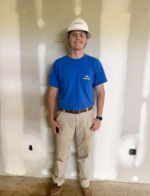 Construction worker in blue shirt standing against an unfinished sheetrock wall.