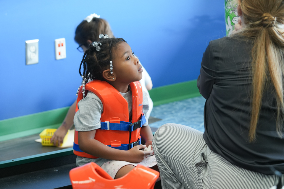Grand Opening of SDPC Academy for Early Learners: student wearing lifejacket in "boat" with teacher