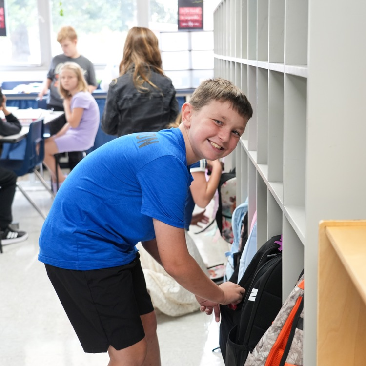 student putting backpack in cubby