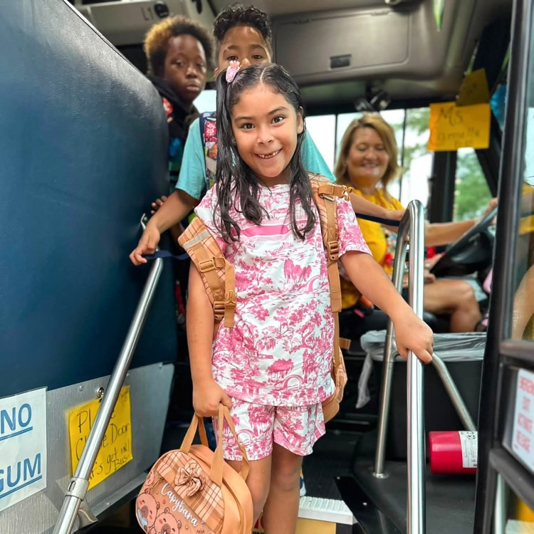 student smiling whiling getting off bus, bus driver smiling behind her