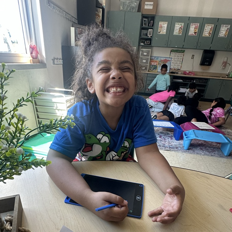 A smiling third grade student in Ms. Bezy’s class holds a stylus while working on a writing tablet during a hands-on compound word activity.