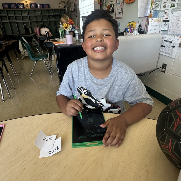 A smiling third grade student in Ms. Bezy’s class holds a stylus while working on a writing tablet during a hands-on compound word activity.