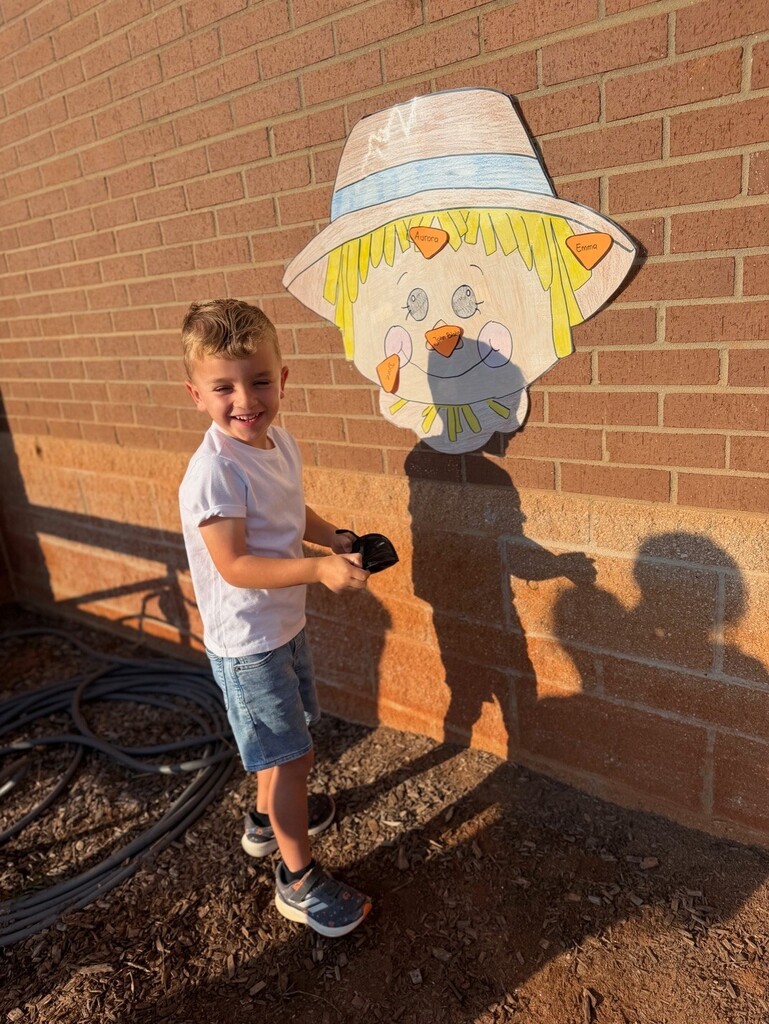 Kindergarten student pinning the nose on the scarecrow.