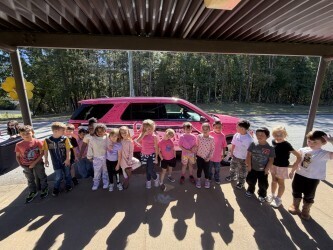students pose next to the pink car