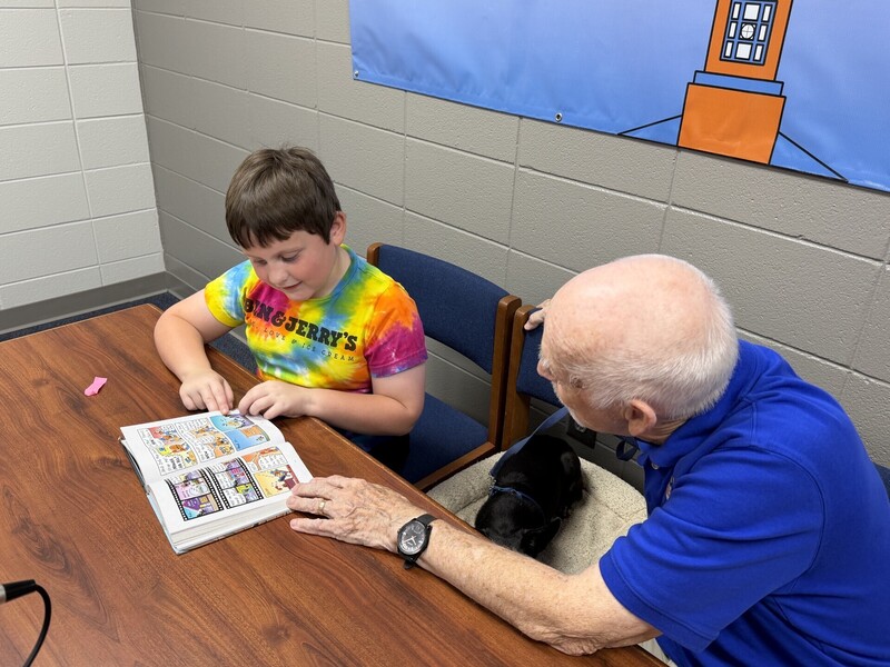 Mr. Jelinek and Dabo enjoying hearing a story being read by a second grade student.