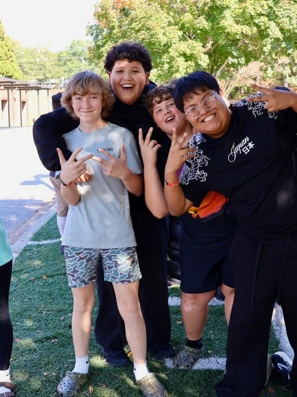 Four middle school students posing and smiling outdoors on a field during a school celebration.
