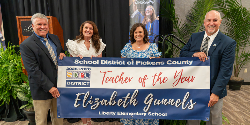 Elizabeth Gunnels standing with Teacher of the Year banner