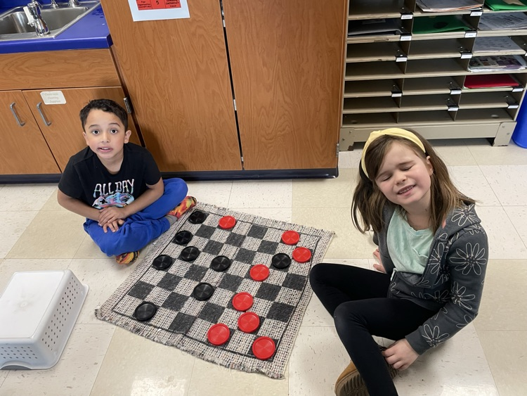 One first grade boy, and one first grade girl playing checkers on the floor