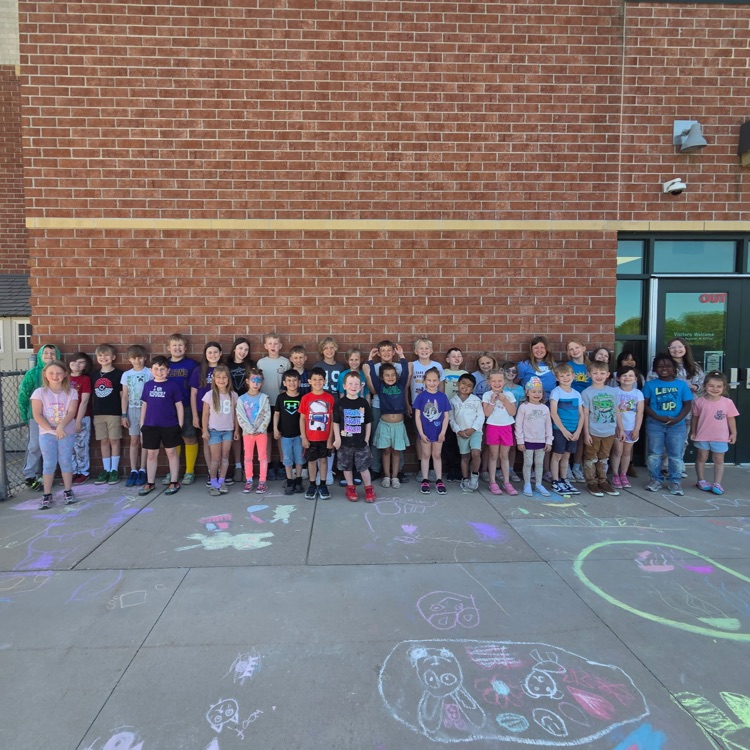 two classes of students standing against the wall behind chalk drawings on the ground