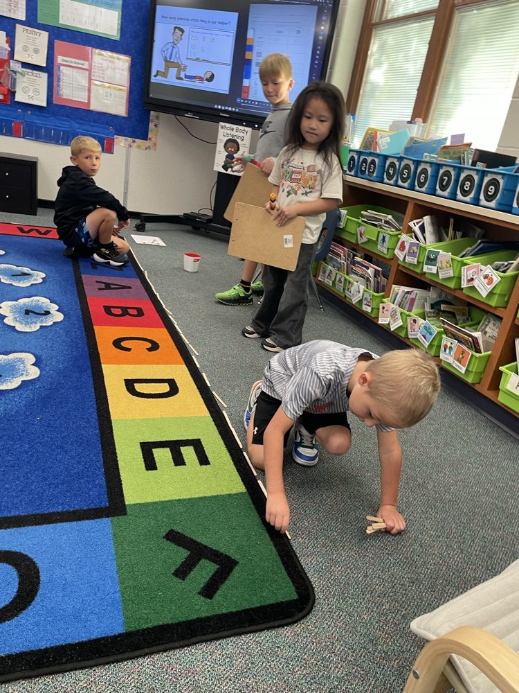 a group of 1st graders measuring the rug with popsicle sticks
