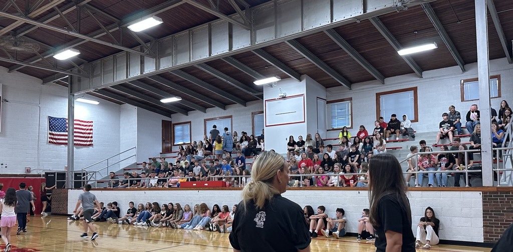 An indoor basketball court with spectators. People are seated and standing. Two women face each other, facing the crowd.