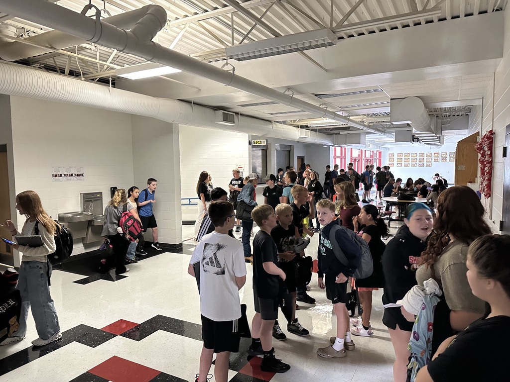 A busy hallway with a diverse group of students standing and talking, some carrying backpacks.