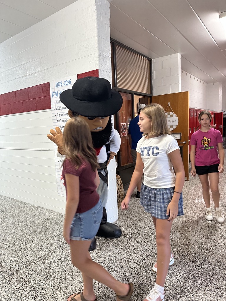 Four students walk through a school hallway. A mascot in front of them wears a black hat.