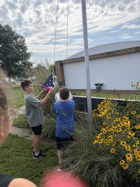 A group of people raises a flag on a pole with a building in the background.