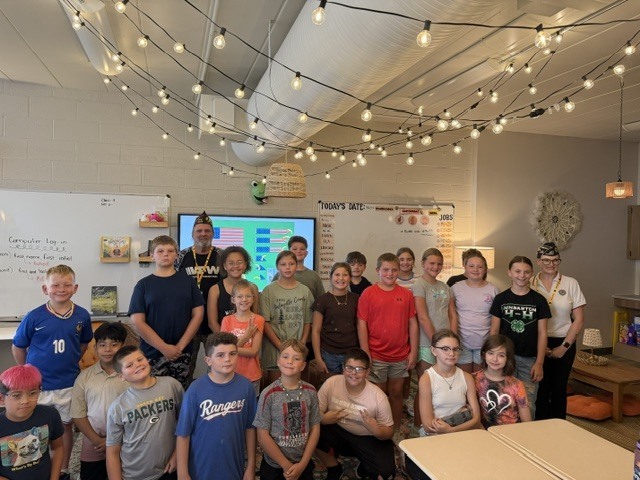 A classroom with students and a teacher posing for a photo with string lights hanging above.