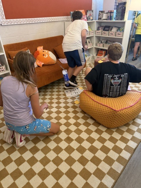 Three children playing on a checkered floor. Two are sitting while the other stands. A couch is in the background.