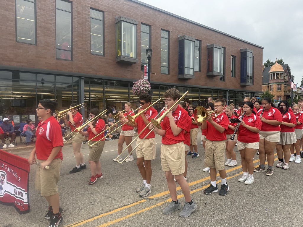 A school marching band plays trombones and tubas in a parade on a city street.