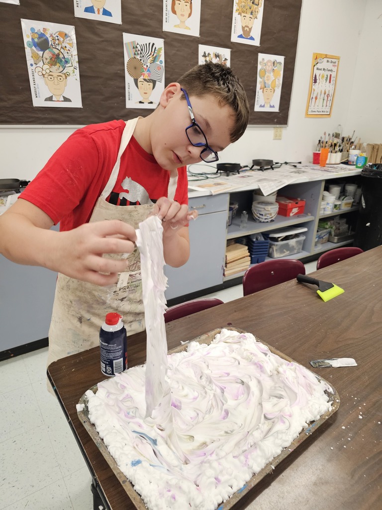 A young person in a red shirt and eyeglasses applies shaving cream to a tray.