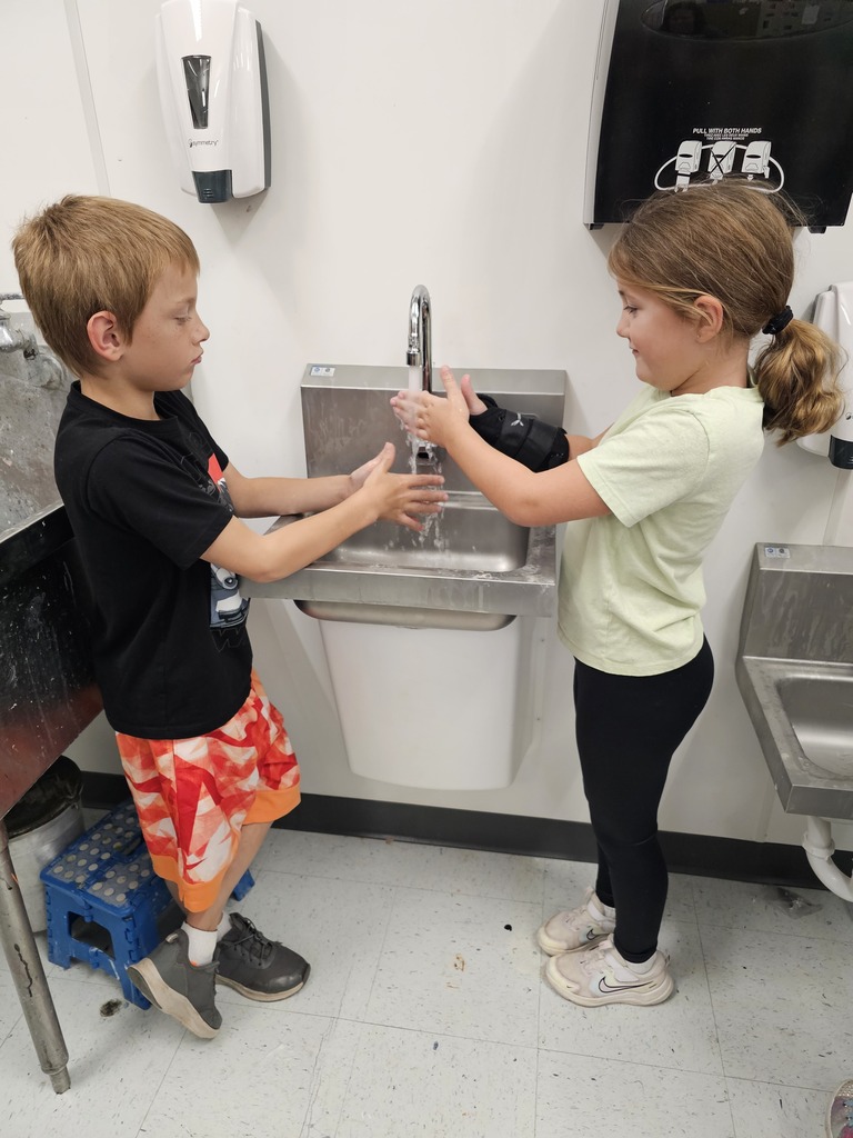 Two kids washing their hands at a sink. A boy is standing by a stool.