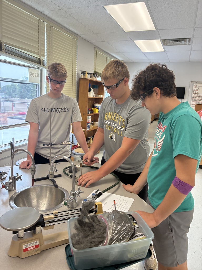 Three students in a lab setting with protective eyewear, working together at a lab table.