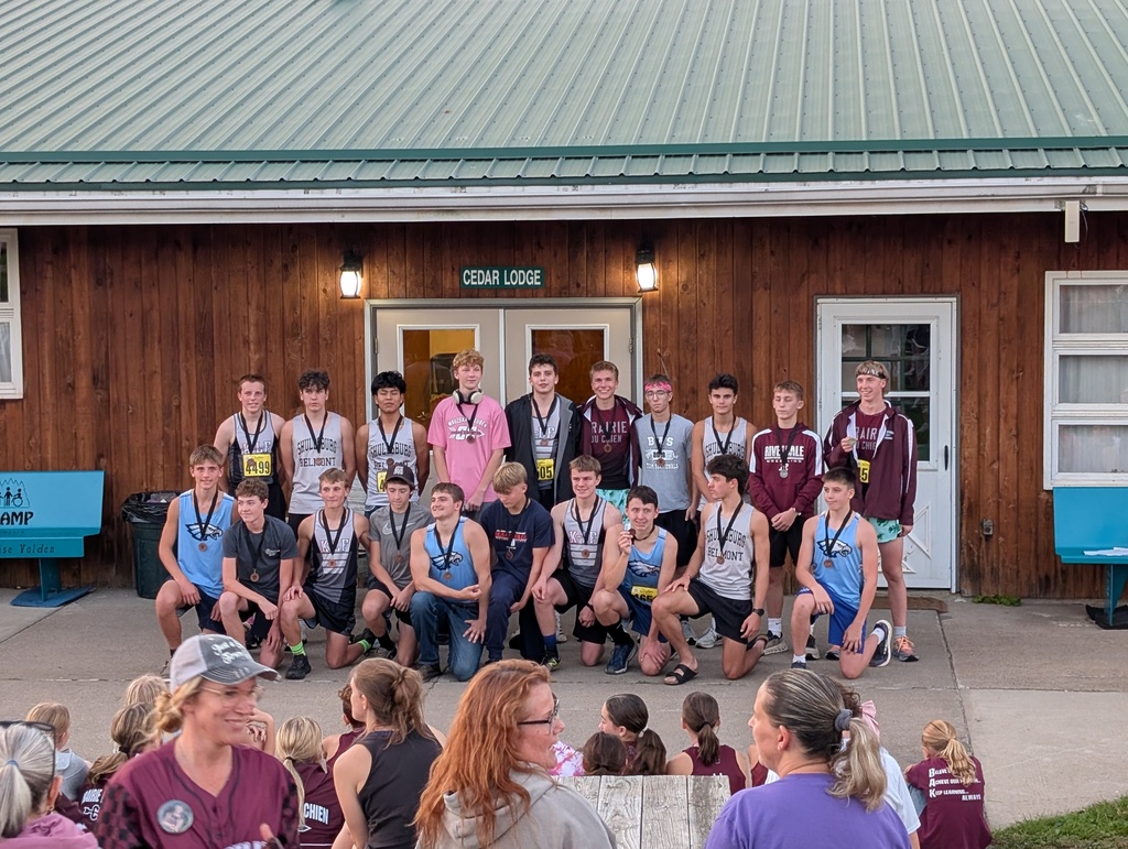 Group of young athletes wearing medals pose in front of a building with a green roof.