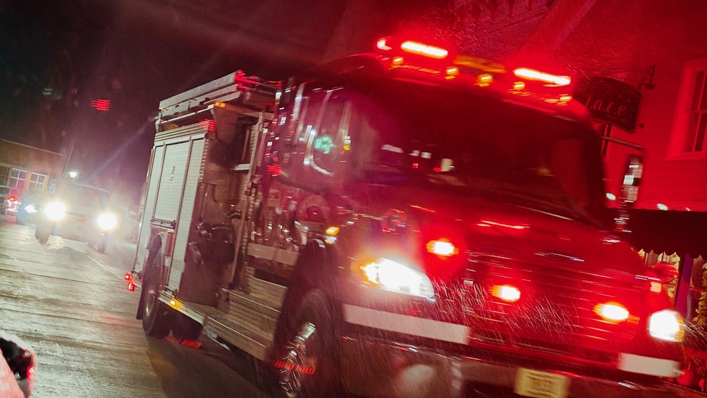 A fire engine with red lights on is driving down a road at night.