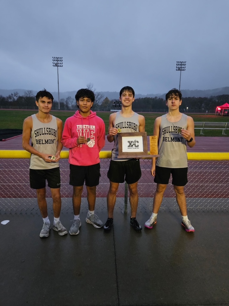 Four young men stand on a track, wearing numbered bibs, holding medals, and one holding a trophy.