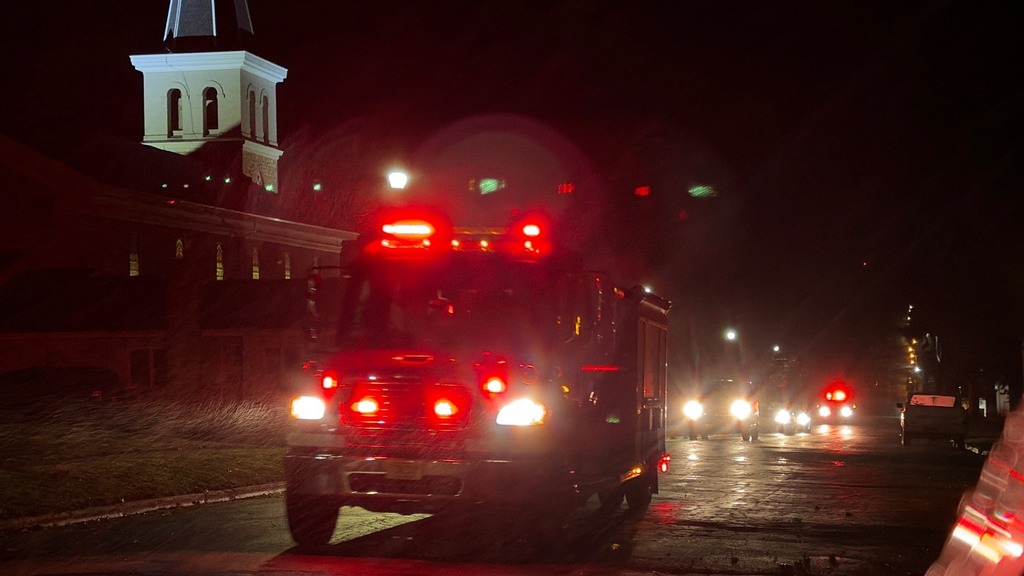 Fire truck with red lights on in front of a building with a steeple at night.