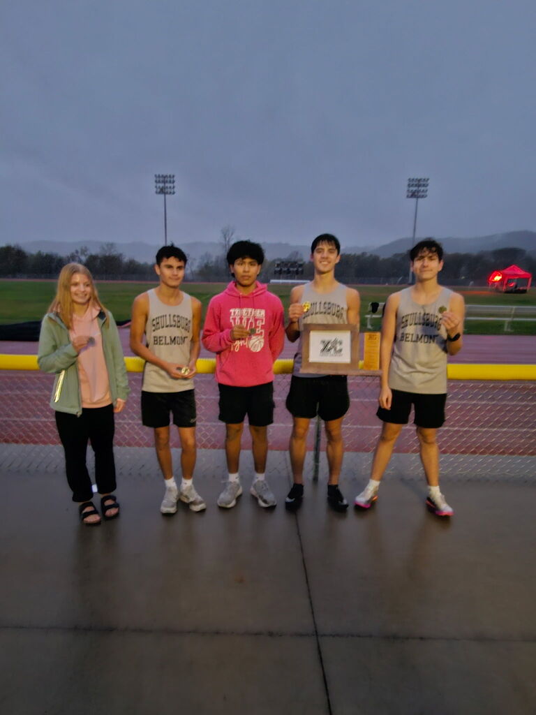 Five individuals pose together at a track event. Three of them hold medals. One man holds a plaque.