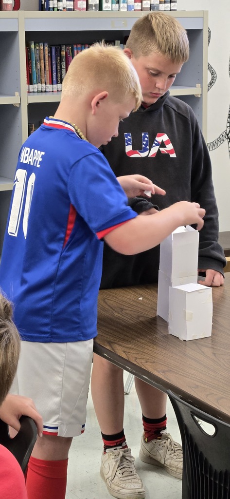Two boys working on a stack of white blocks on a table in a classroom.