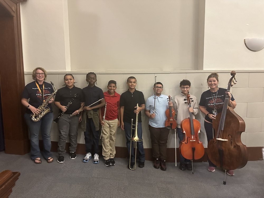 District staff members and students holding up instruments in a middle school auditorium.
