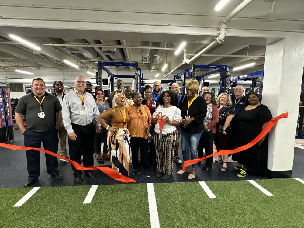 School Board, District, and School Leaders, gather behind a red ribbon for the Ribbon Cutting Ceremony in the new weight room