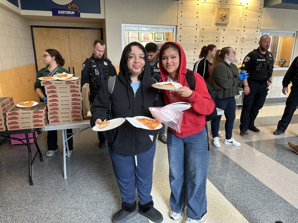 Two students smiling and holding up pizza