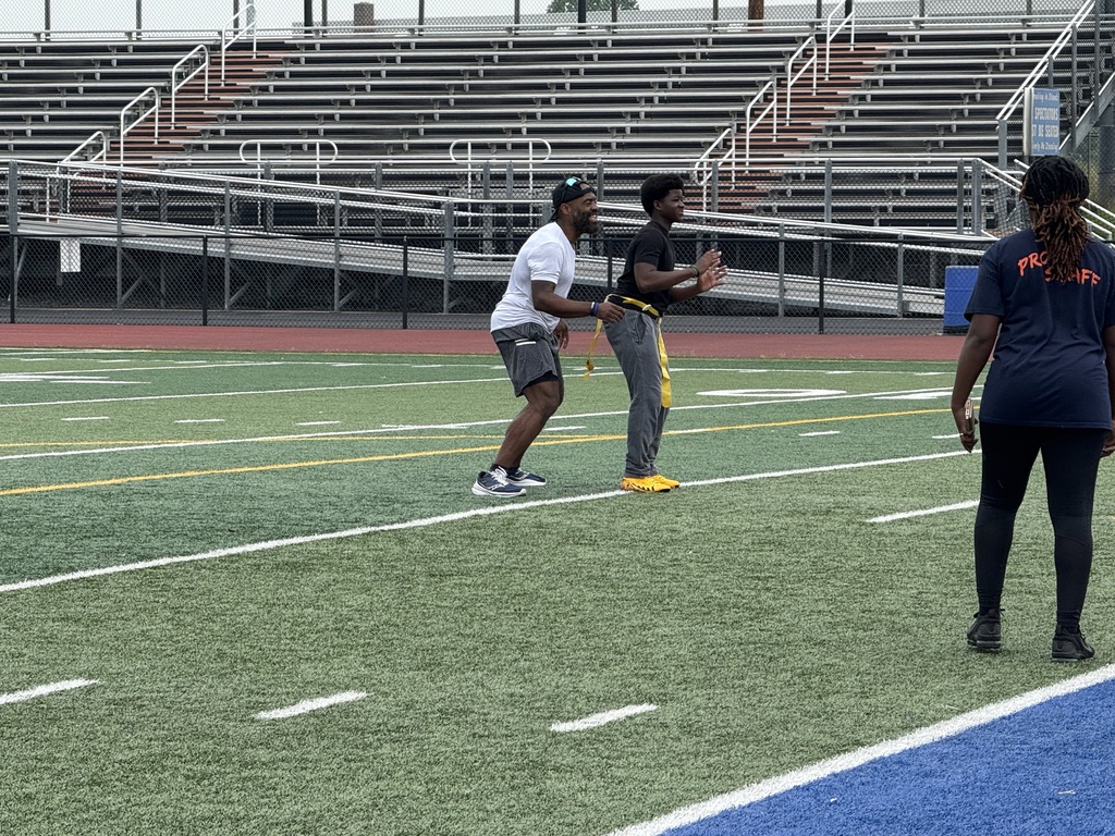 Two people standing next to each other on a sports field with another person standing from afar