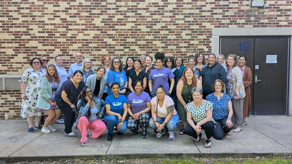 A diverse group of women and one man poses together in front of a brick wall, showcasing a sense of community and friendship.