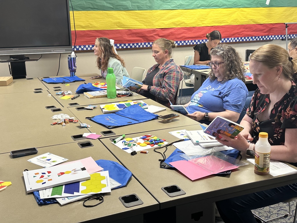 A group of participants engaged in a workshop at a table filled with educational materials, books, and colorful learning tools.