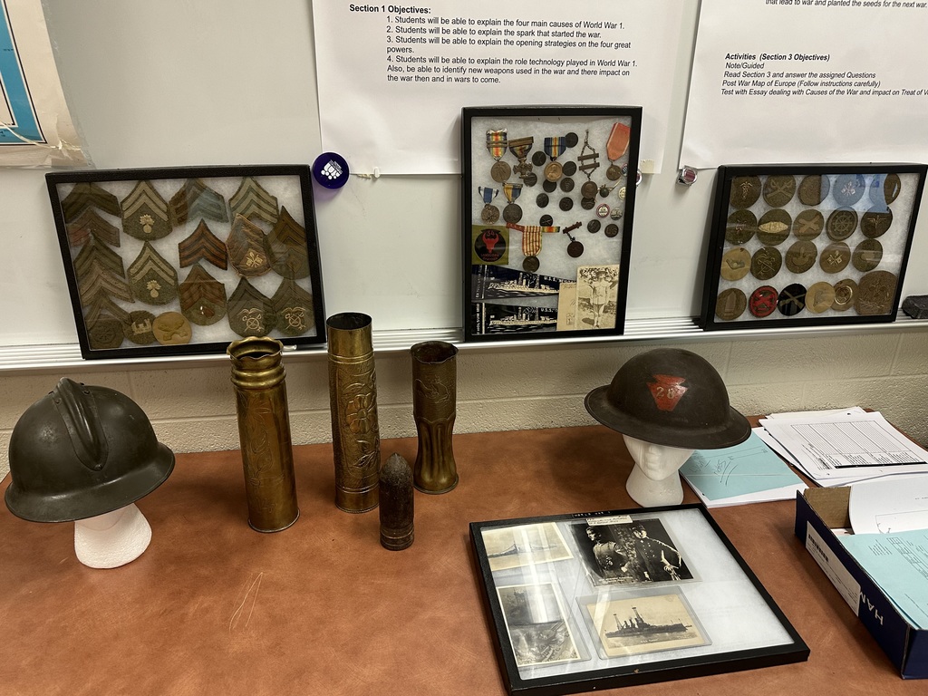 A display of military memorabilia including medals, badges, helmets, and historical photographs arranged on a table.
