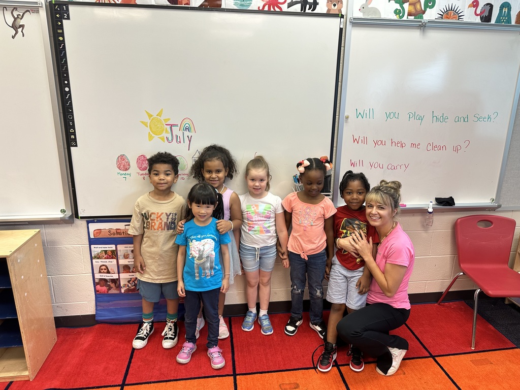A teacher and a group of students standing on a carpet in a classroom.
