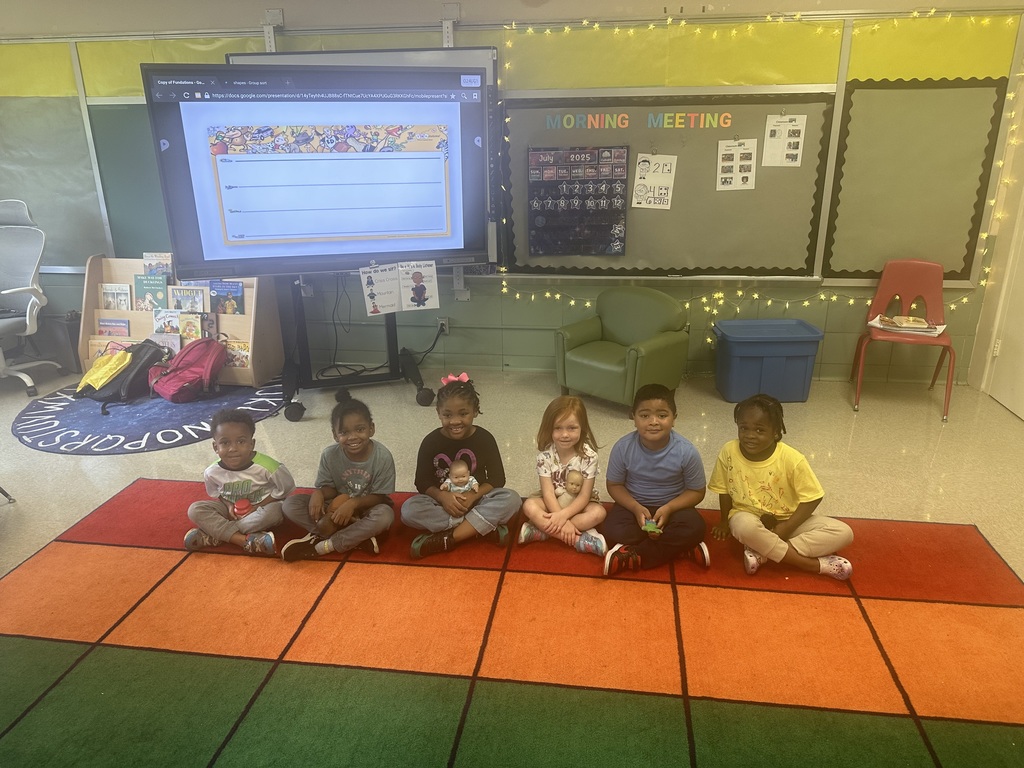 A group of students sitting on a carpet in a classroom holding a toy.