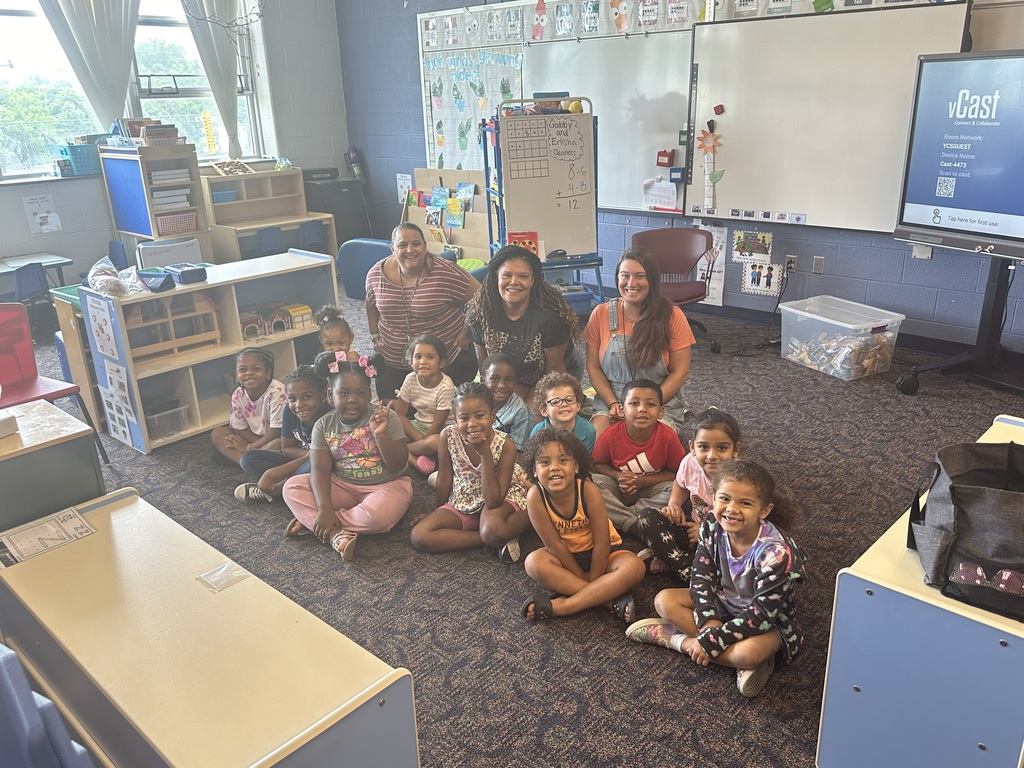 A group of students and three teachers sitting on a carpet in a classroom.