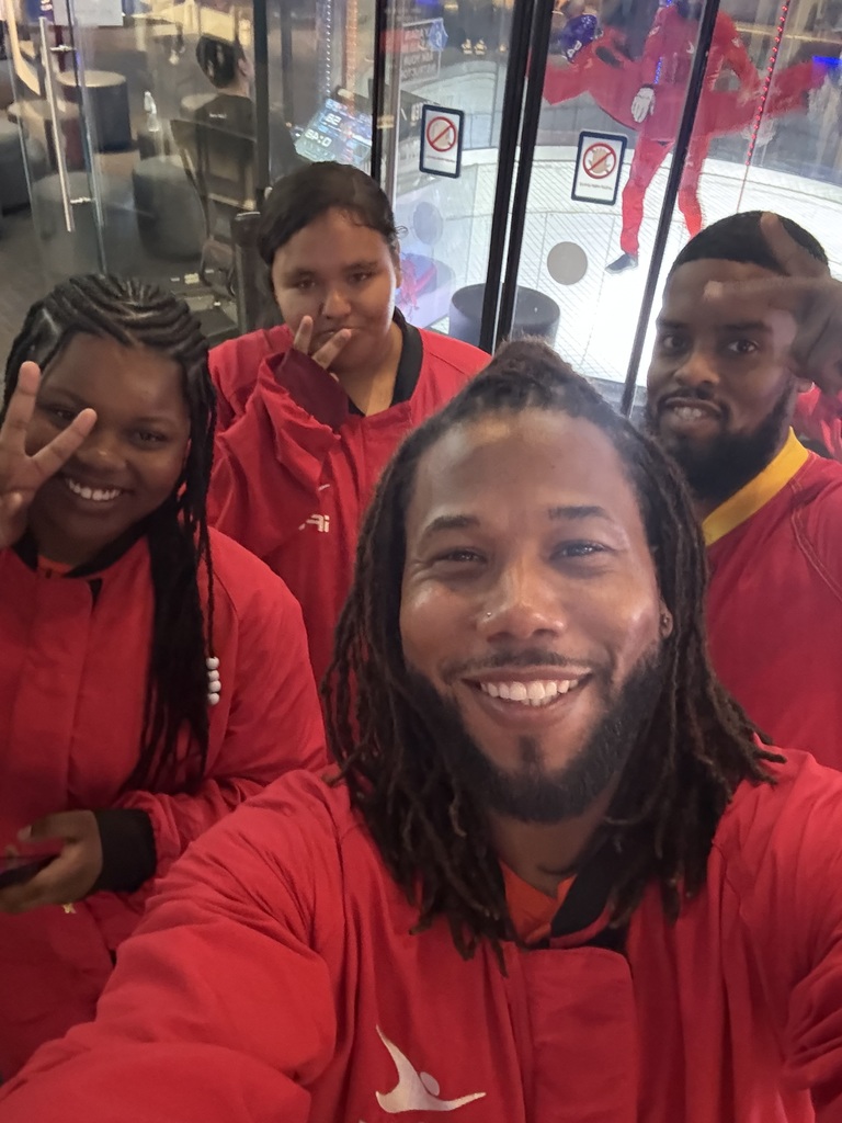 Two adults and two students posing for a selfie. Both students and one of the adults are holding up the peace sign.