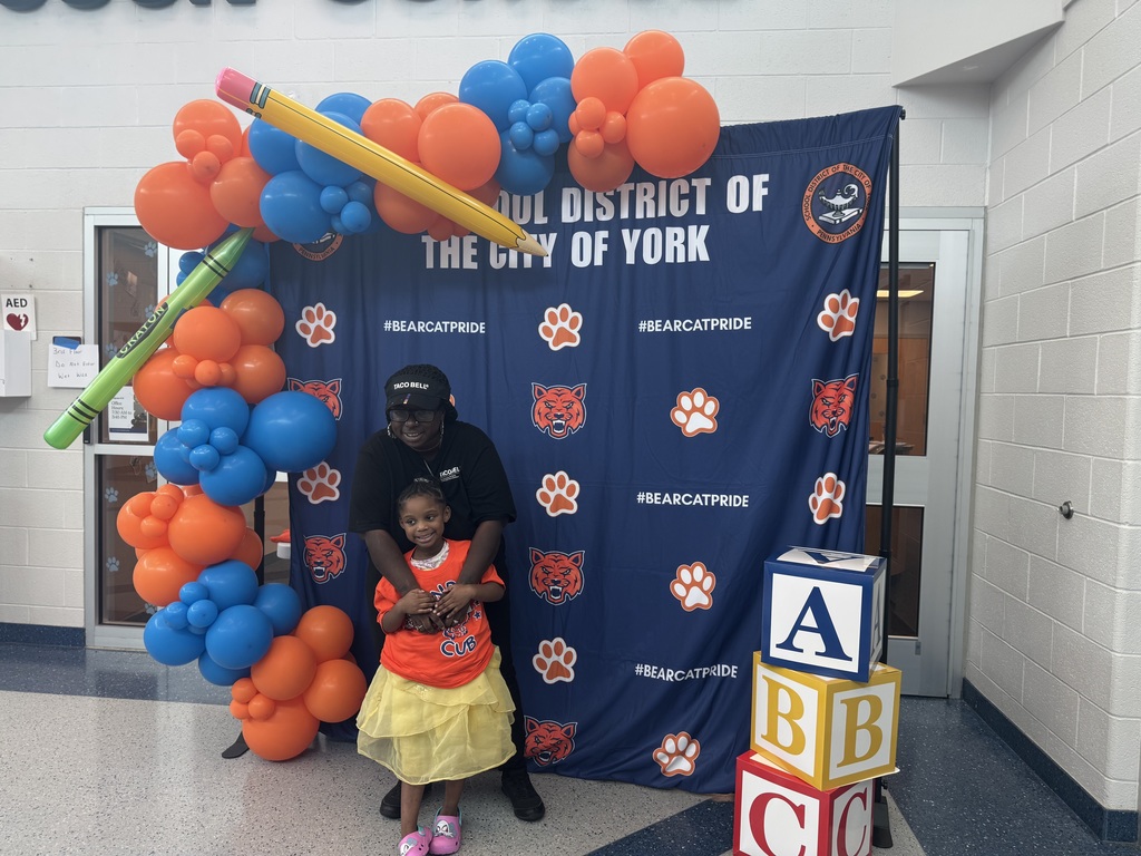 A parent and an incoming Kindergarten student pose in front of a orange and blue backdrop with the words "The School District of the City of York" on it during Ferguson PreK-8's recent Kindergarten Orientation event.