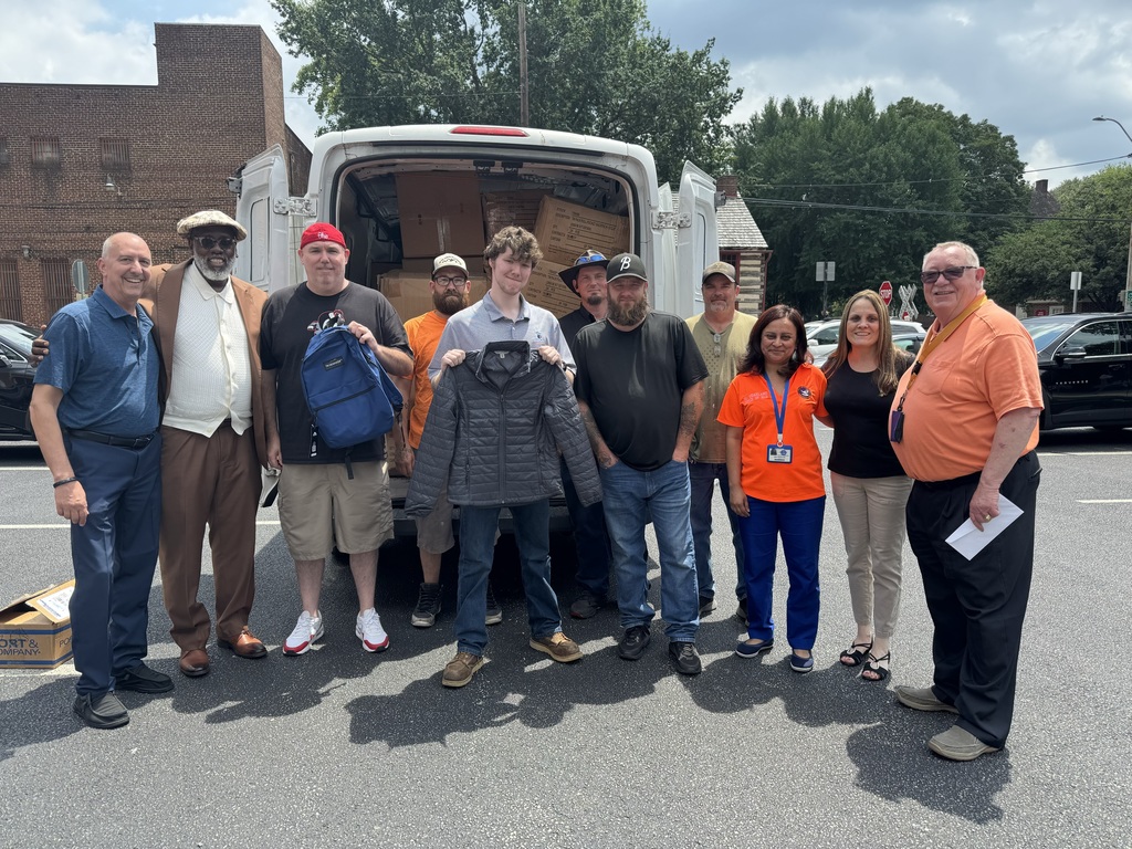 District staff received bookbags and coats from employees at Statewide Partners. One of the employees is holding a backpack and another employee is holding a jacket.