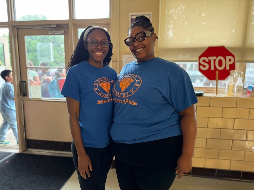 District staff at Devers PreK-8's Back to School Night. A student can be seen walking outside in the background. 